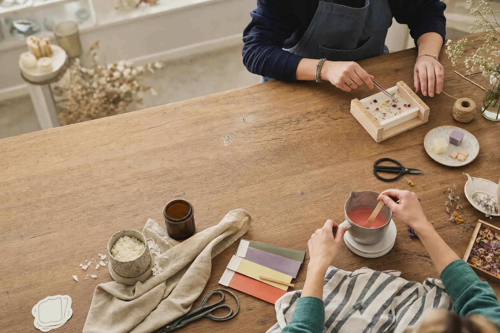 Two adult makers working with wax, botanicals and colour at a shared craft table